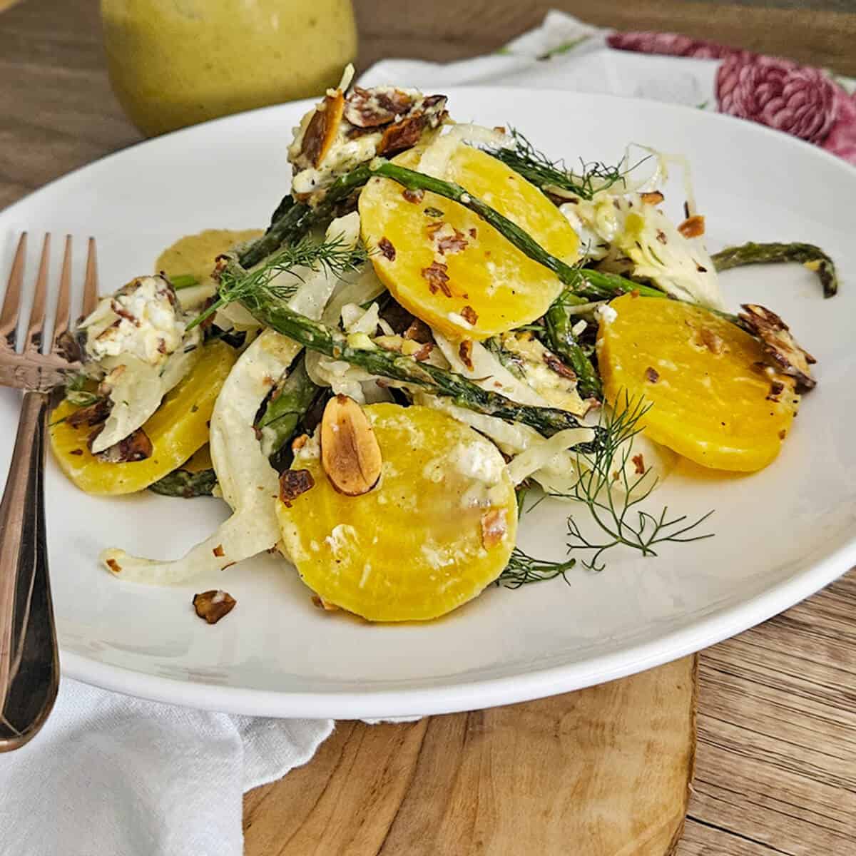 Roasted asparagus and fennel salad with golden beets on a plate with a fork and charred lemon salad dressing in a glass jar with a spoon.