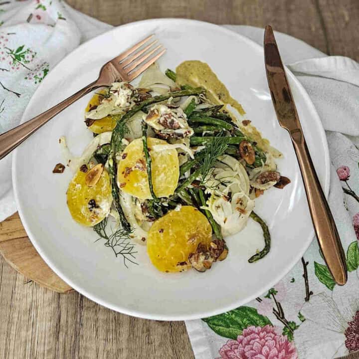 Roasted asparagus and fennel salad with golden beets on a plate with a fork and knife.