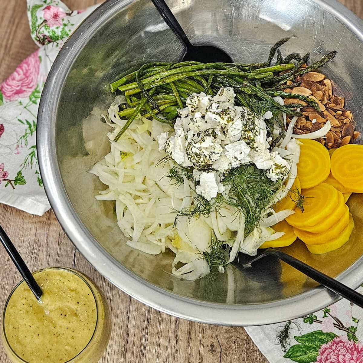 The ingredients for roasted asparagus and fennel salad in a mixing bowl with utensils, and charred lemon salad dressing in a glass jar with a spoon.
