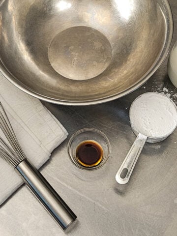 A metal bowl, whisk, and the cream, sugar, and vanilla for the whipped cream.