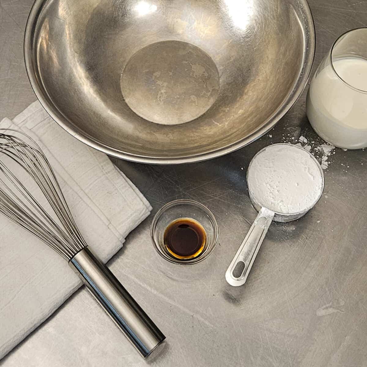 A metal bowl, whisk, and the cream, sugar, and vanilla for the whipped cream.