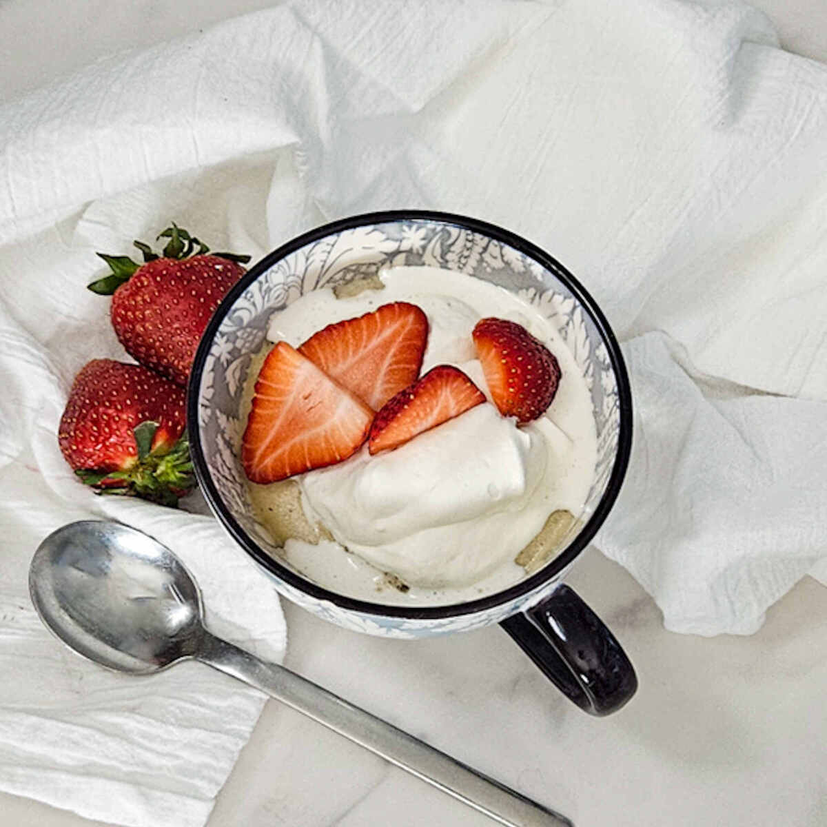 Strawberries and cream mug cake in a mug with fresh strawberries.