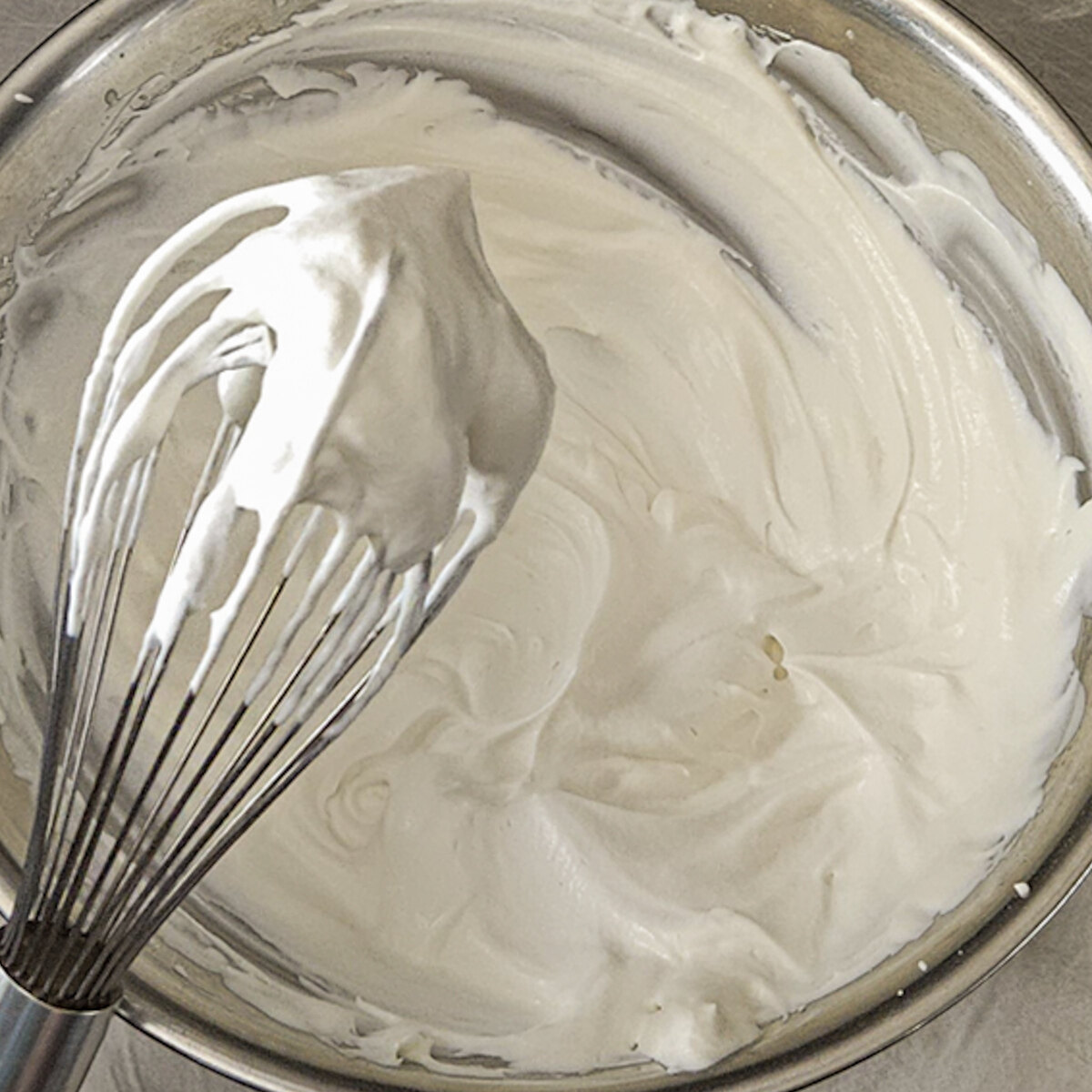 Whipped cream in a bowl with a whisk.