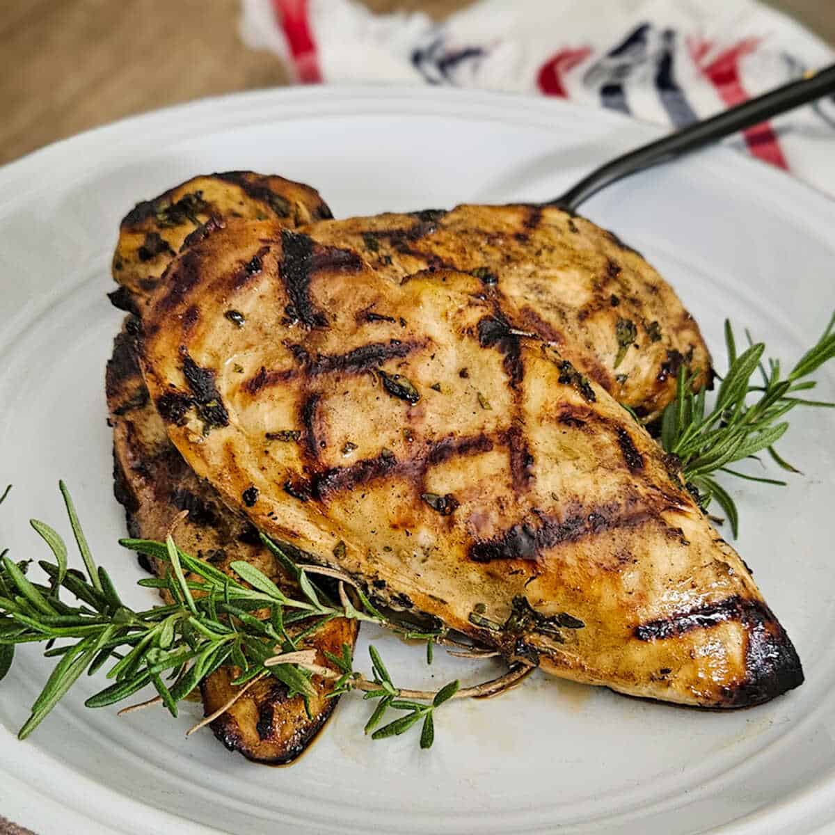 Grilled white balsamic herb chicken breast with rosemary sprigs on a white plate.