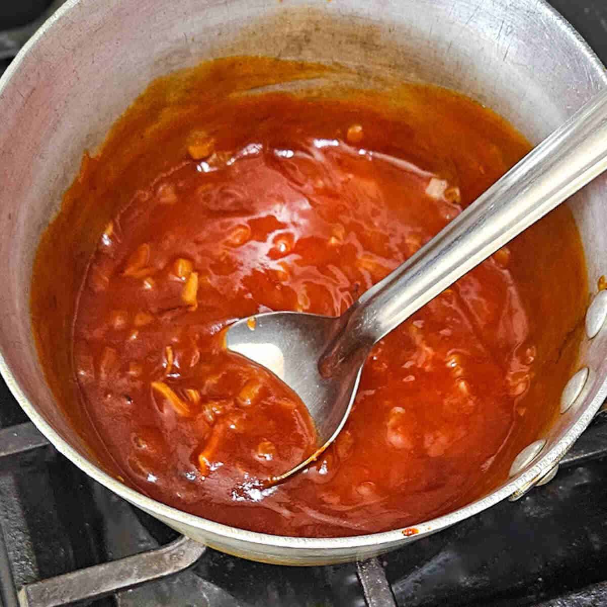 A metal pot with sauce and a spoon.