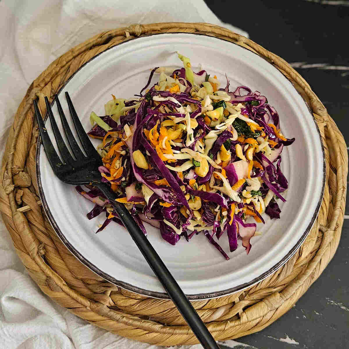 A plate of crunchy Thai style slaw with peanuts and lime with a fork.