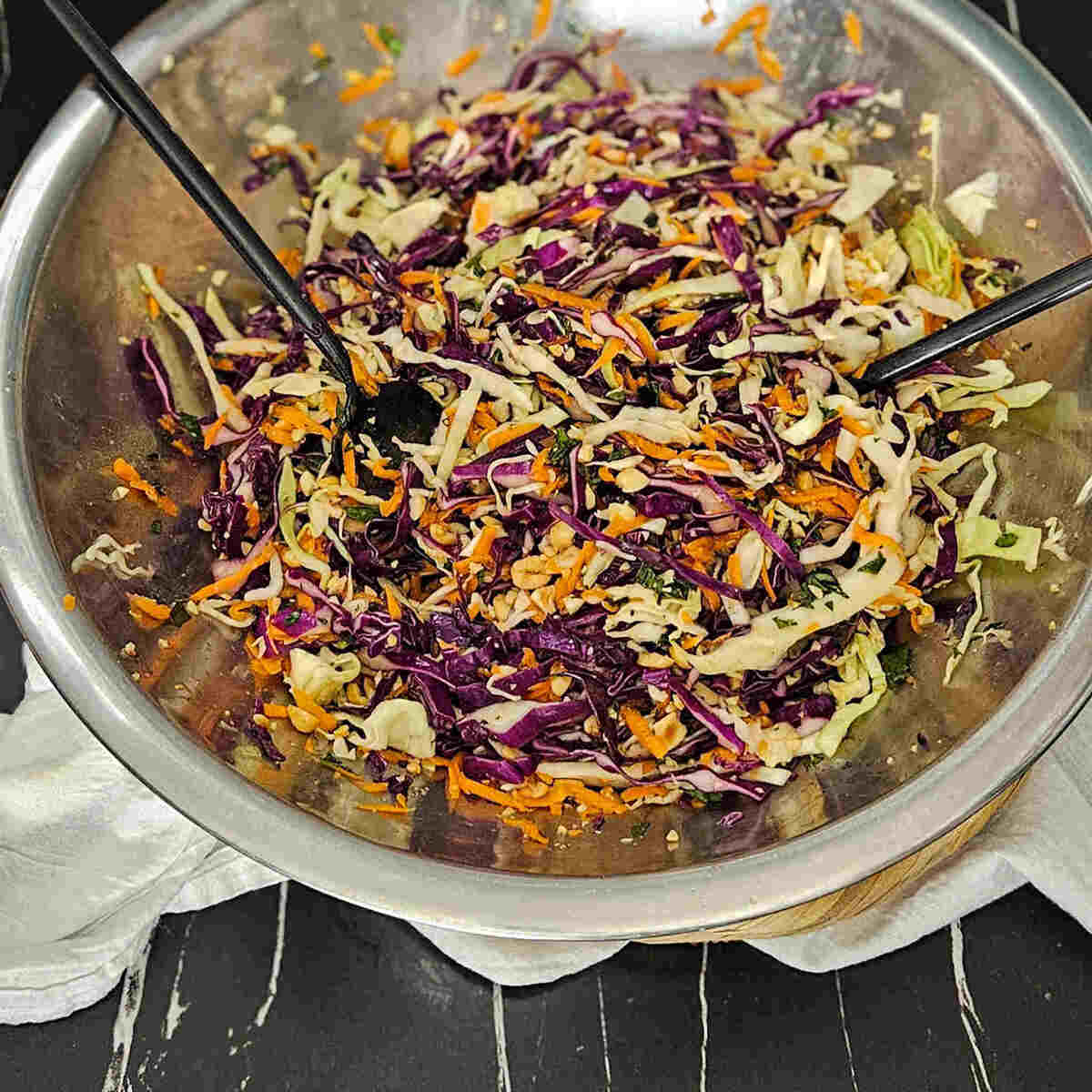 A bowl of crunchy Thai style slaw with black serving spoons.