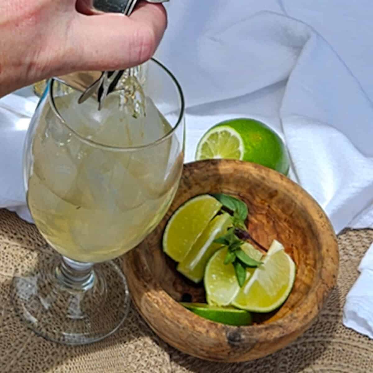 A person is pouring a drink into a glass with lime slices.