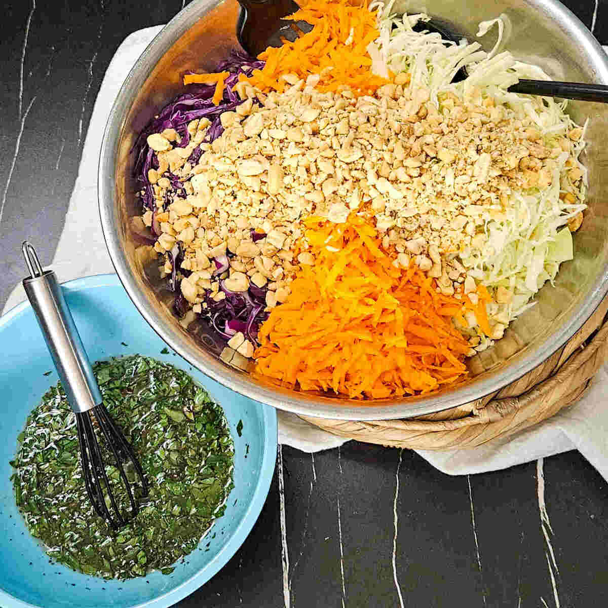 A bowl of Thai style slaw with a whisk and a bowl of dressing.