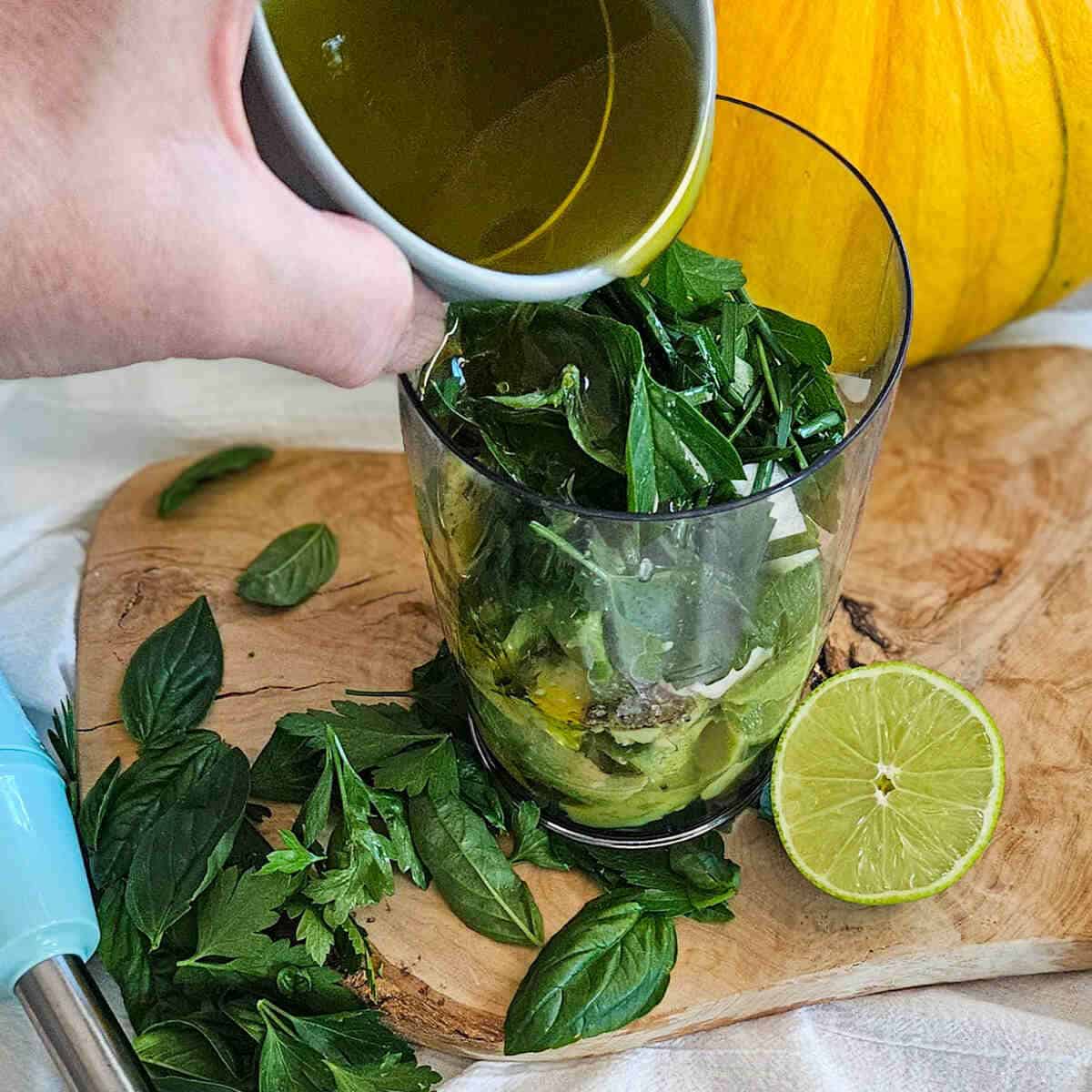 Fresh basil leaves in a glass with lime and avocado and olive oil preparation for creamy avocado salad dressing.