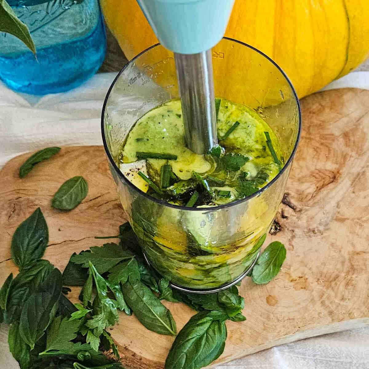 Fresh herb and avocado salad dressing in a pitcher being blended on a wooden surface