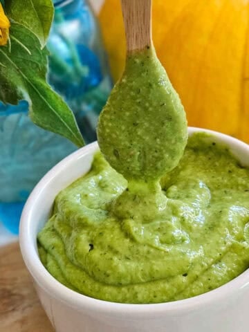 Creamy avocado dressing in a white bowl with a wooden spoon for dipping