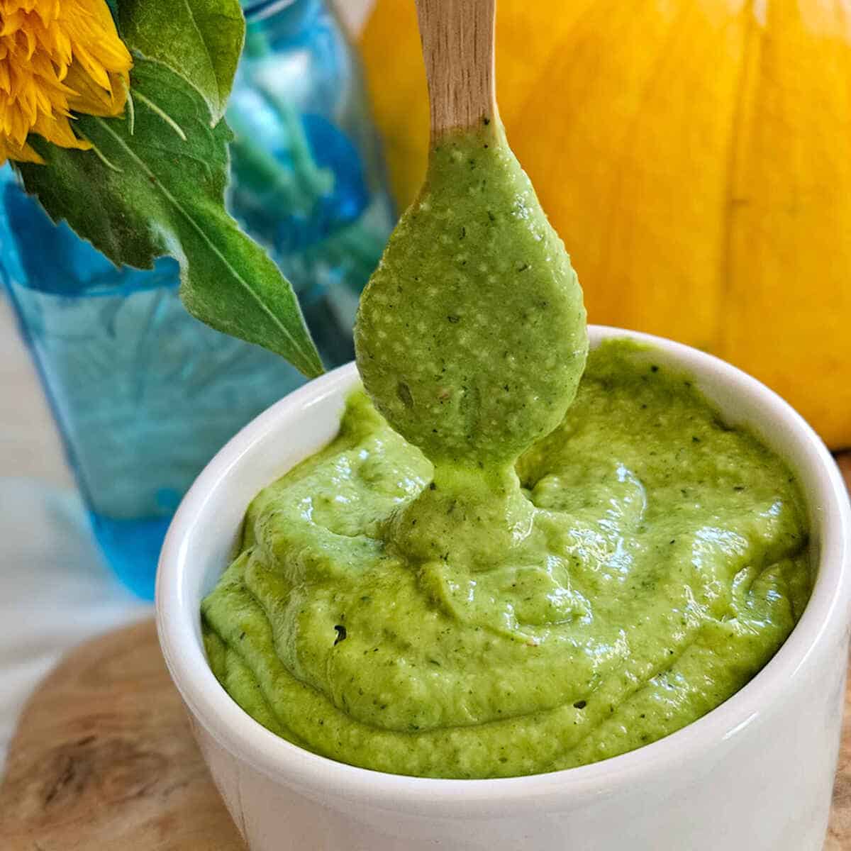 Creamy avocado salad dressing in a ramekin with a coated wooden spoon.