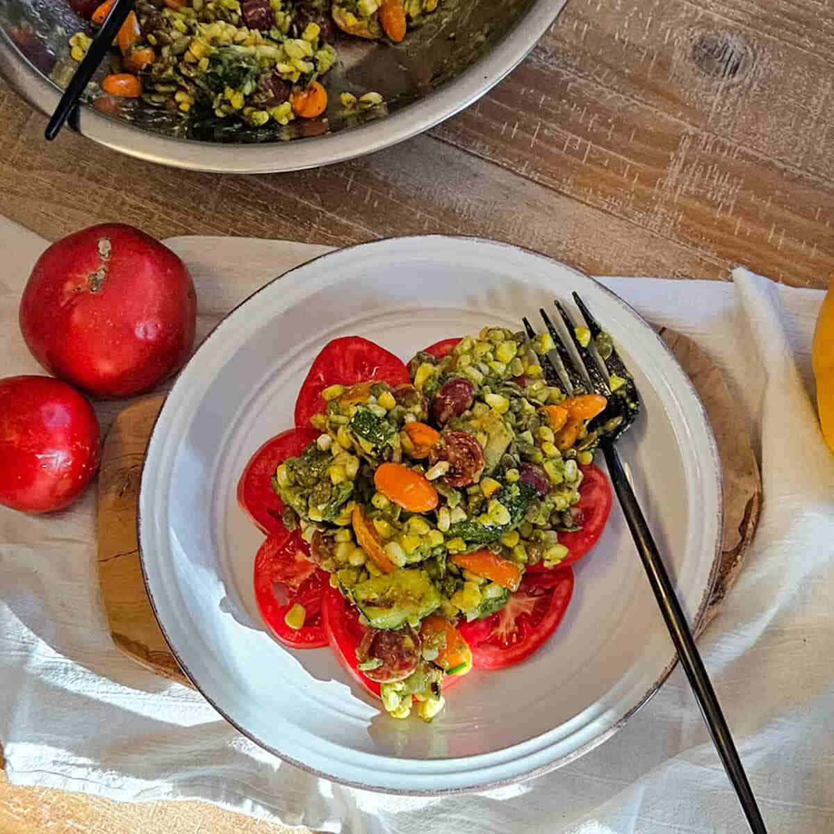 Vegan corn and tomato salad served on a white plate with sliced tomatoes, garnished with fresh vegetables, on a rustic wooden table.