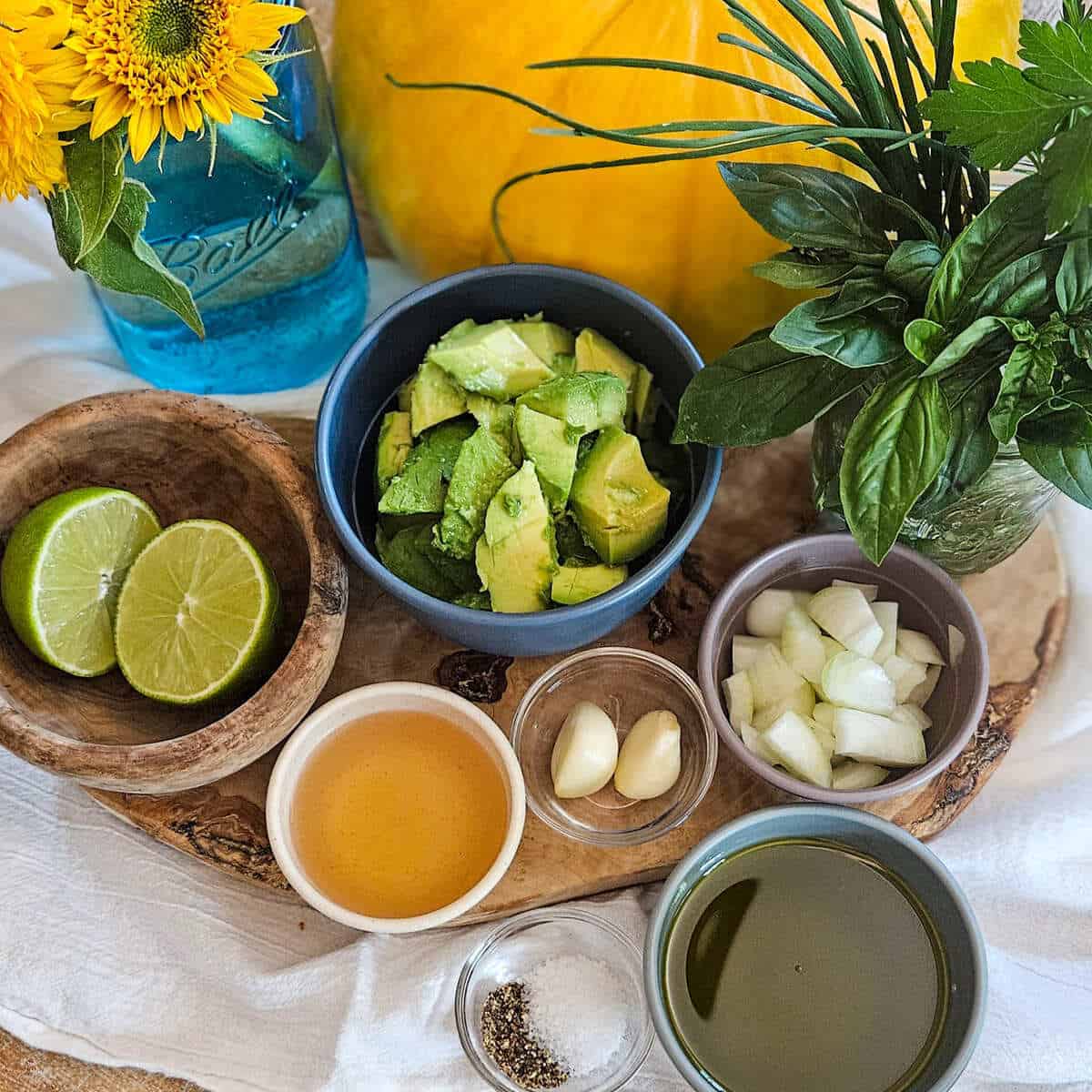 Fresh avocado chunks and ingredients for creamy avocado dressing, with lime, garlic, and herbs on a rustic kitchen tray.