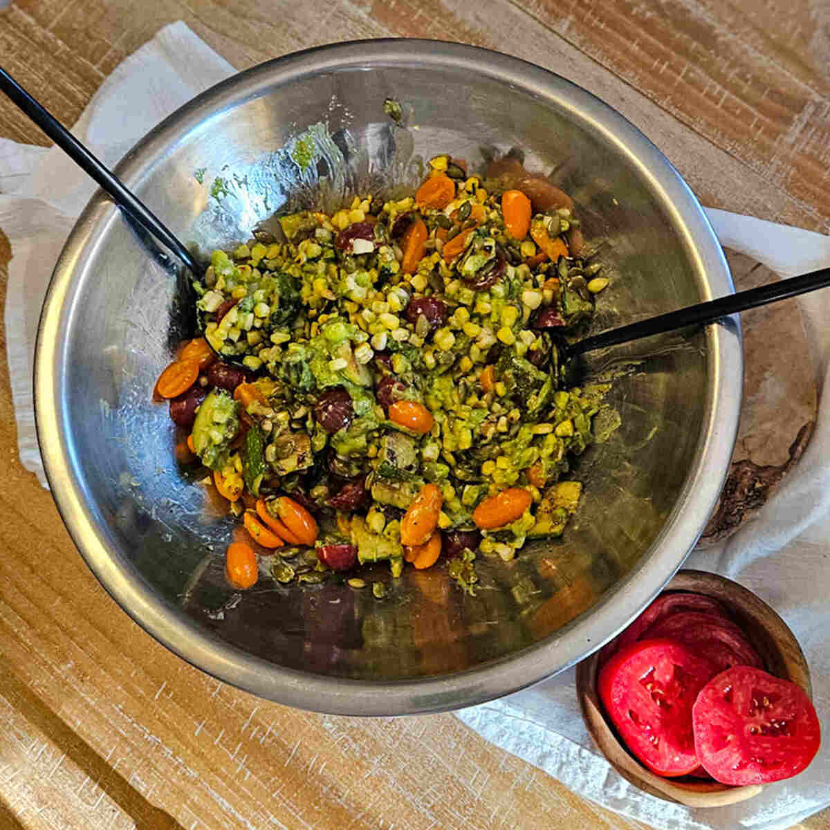 Roasted vegetable medley in a stainless steel bowl with fresh tomatoes on side