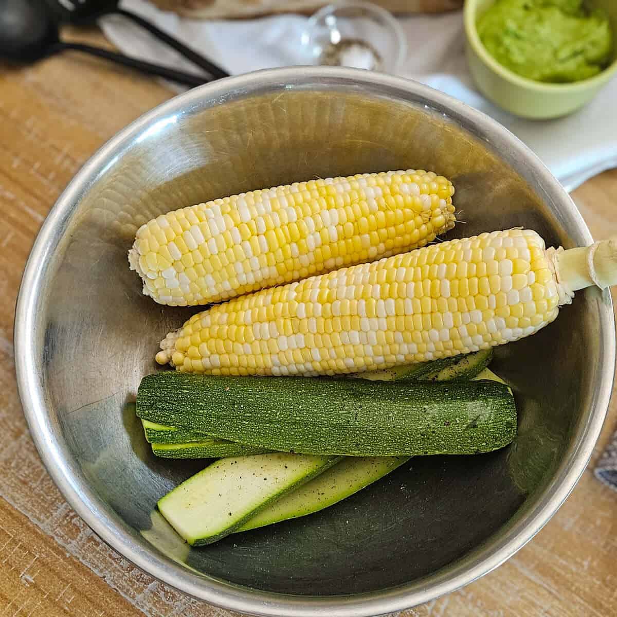 sweet corn and zucchinis in stainless steel bowl for seasonal ingredient preparation