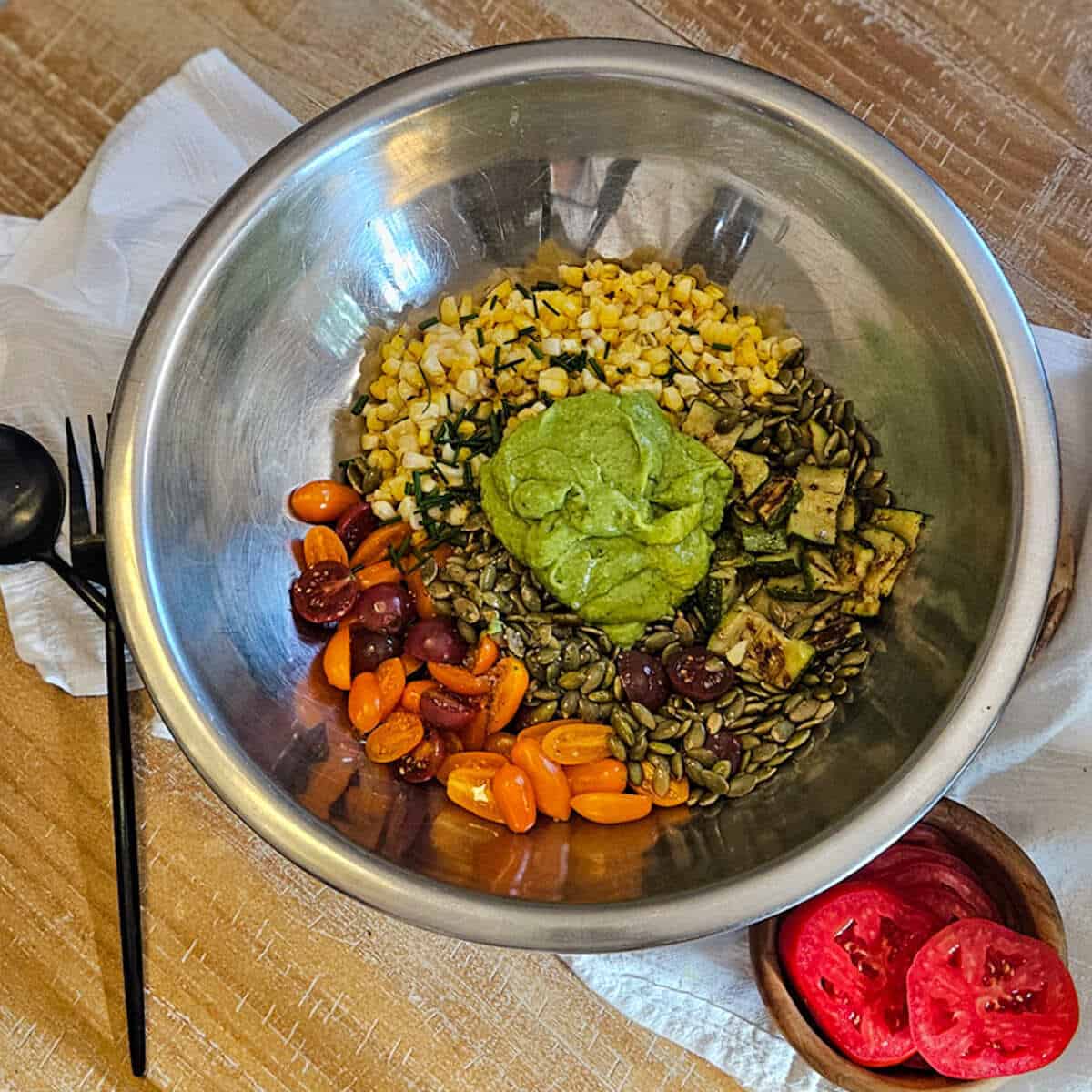 Fresh garden salad ingredients for season two taste, including corn, cherry tomatoes, creamy avocado dressing pumpkin seeds, and sliced tomatoes.