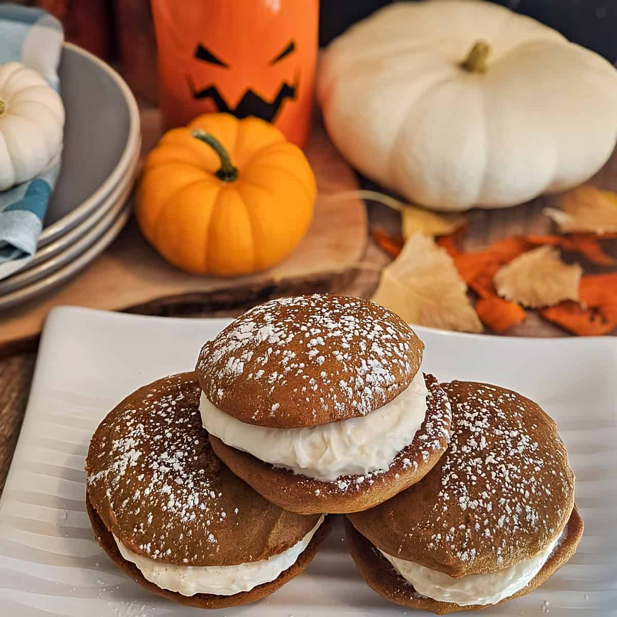 Pumpkin spice whoopie pies with cream filling and autumn-themed decorations, perfect for fall treats and seasonal desserts.