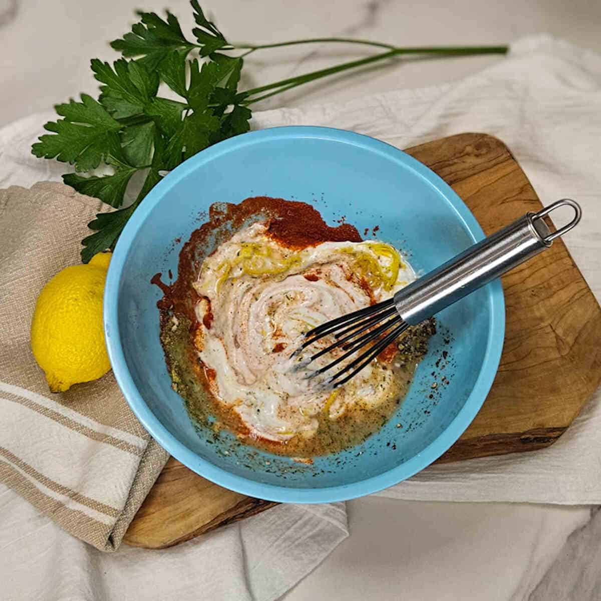 Creamy Greek yogurt marinade in a blue bowl with lemon and fresh herbs, ready for cooking or serving.
