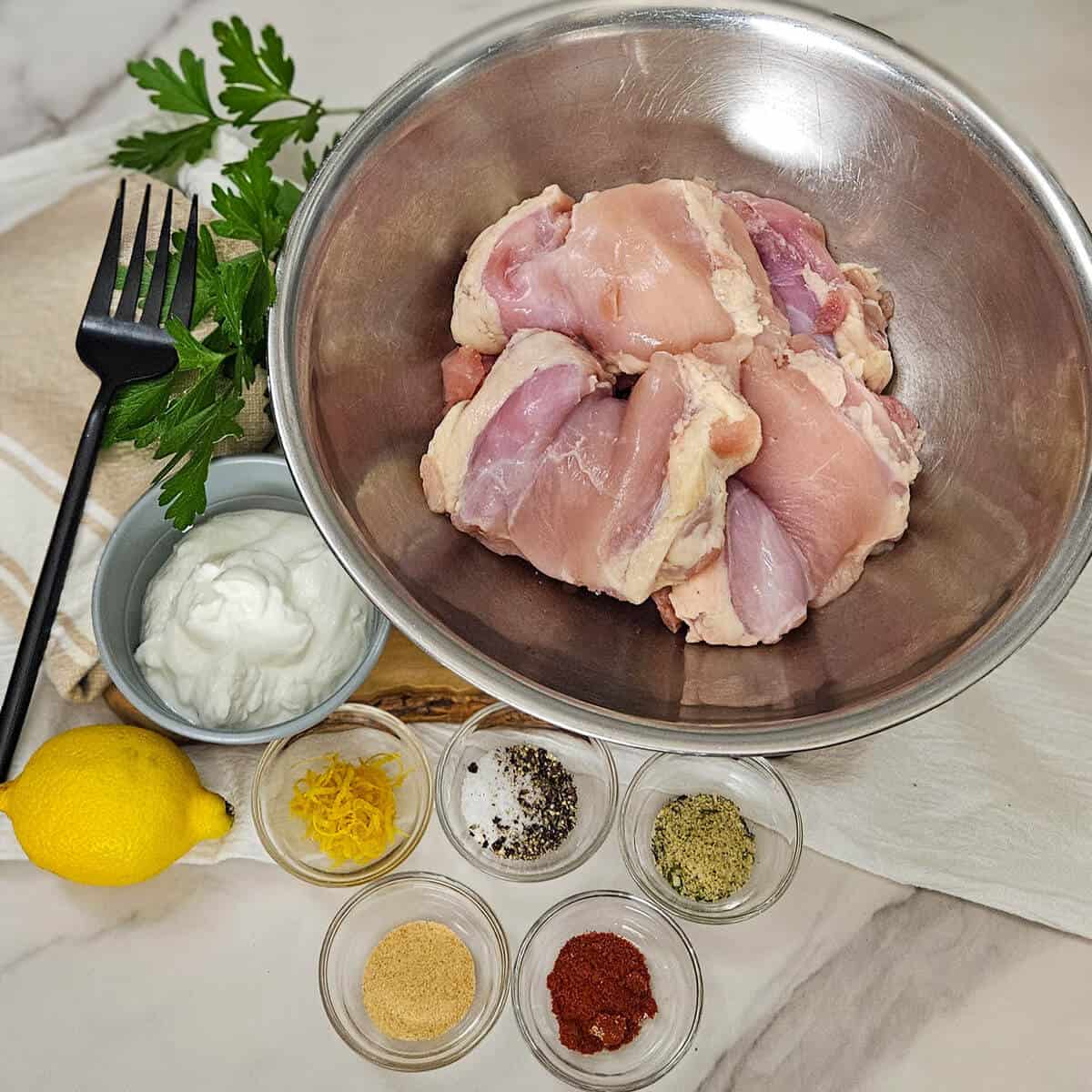 Raw chicken pieces in a mixing bowl with herbs and spices for making grilled Greek yogurt marinated chicken thighs