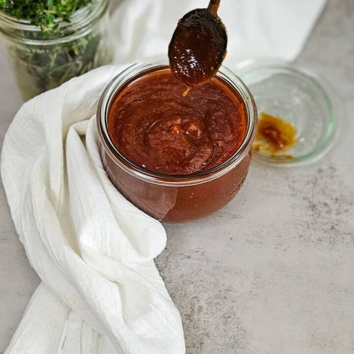 Smooth homemade Kansas city barbecue sauce in a glass jar with a spoonful for dipping or cooking.