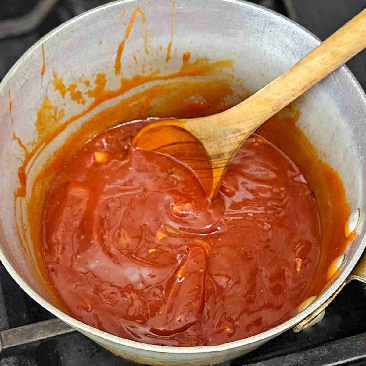 Smooth Kansas city BBQ sauce cooking in a pot with a wooden spoon, perfect for flavorful recipes.