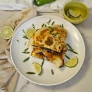 Golden-brown quesadilla with black beans and melted cheese, garnished with lime wedges and fresh herbs.