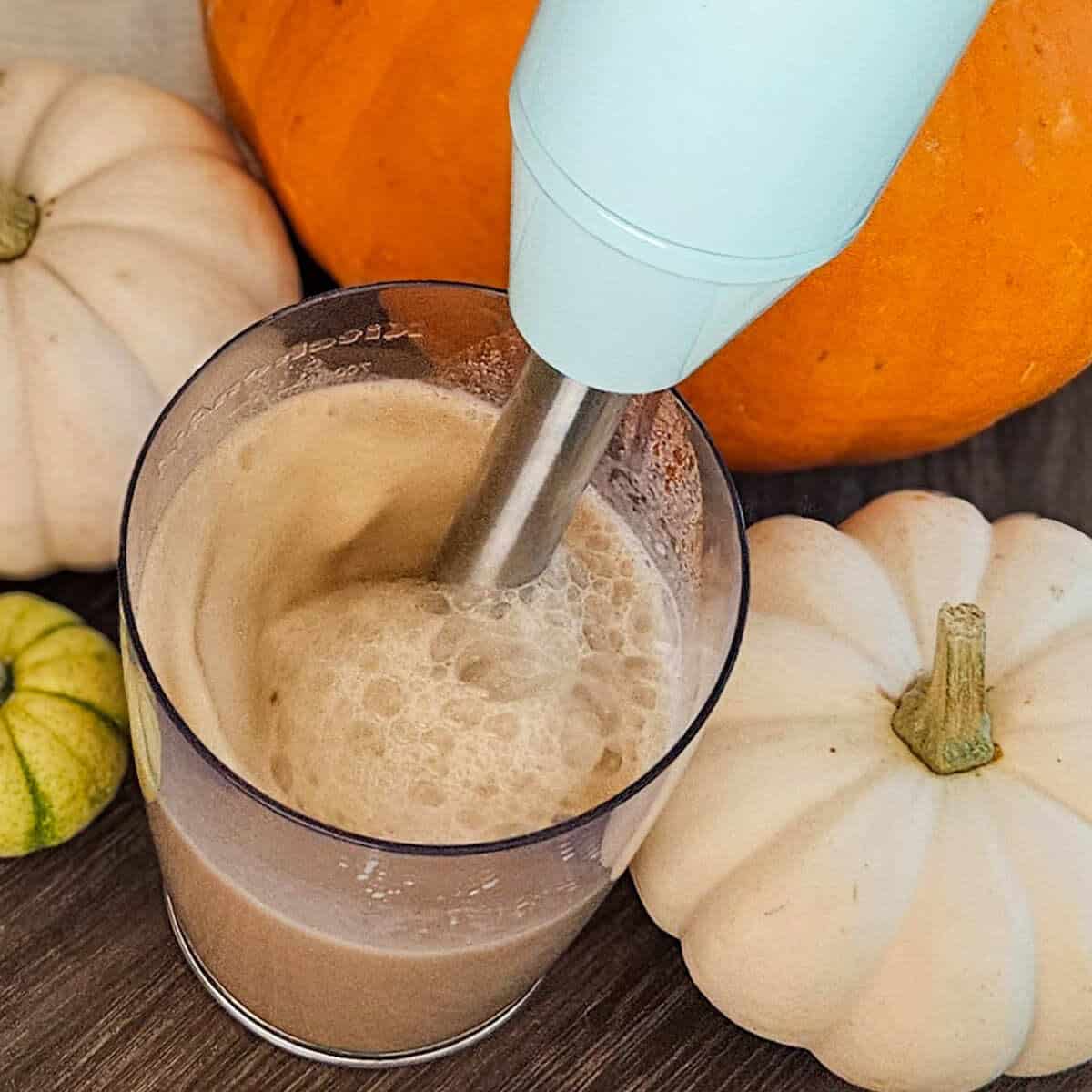 Creamy pumpkin spice latte with an immersion blender surrounded by pumpkins for seasonal flavor.
