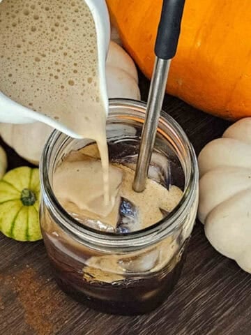 Creamy pumpkin cold brew coffee with fall pumpkins and gourds, perfect for autumn seasonal beverages.