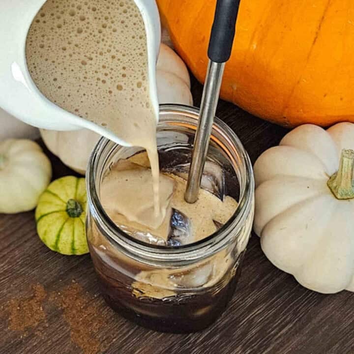 Creamy pumpkin cold brew coffee with fall pumpkins and gourds, perfect for autumn seasonal beverages.