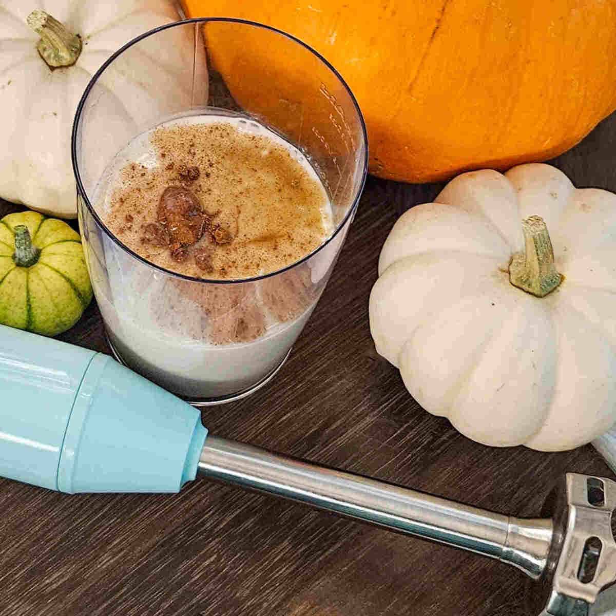 Creamy pumpkin spice oat milk creamer surrounded by white and orange pumpkins. Perfect fall beverage.