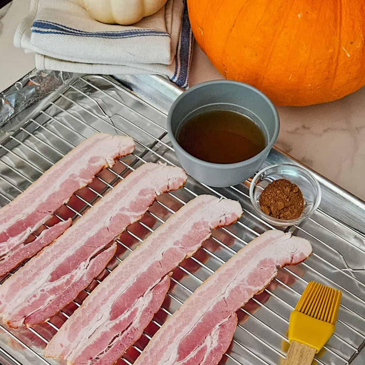 Crispy bacon strips on a wire rack with pumpkin spice seasoning, maple syrup, and autumn pumpkins in the background.