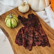 Pumpkin spice bacon on a wooden serving board with decorative mini pumpkins.