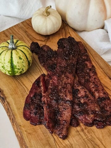 Pumpkin spice bacon on a wooden serving board with decorative mini pumpkins.