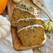 Pumpkin loaf with pumpkin seeds and icing on wooden serving board for seasonal autumn dessert.
