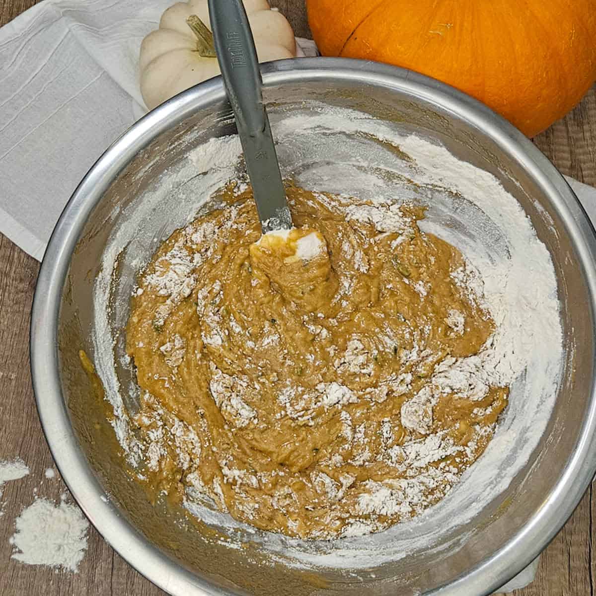 Adding the flour to the pumpkin spice zucchini bread batter in a bowl.
