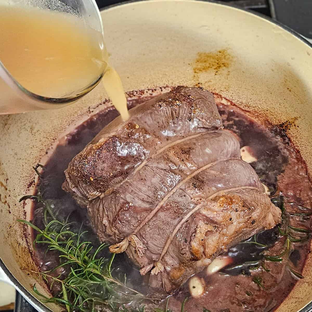 Juicy beef stew cooking with herbs, adding broth in a skillet for rich flavor.