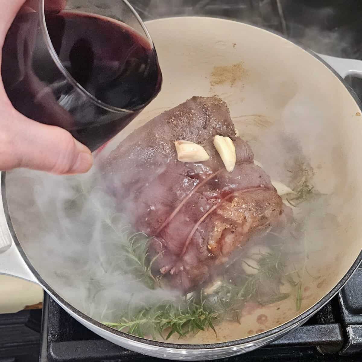 Adding red wine to the pot for red wine braised beef pot roast.