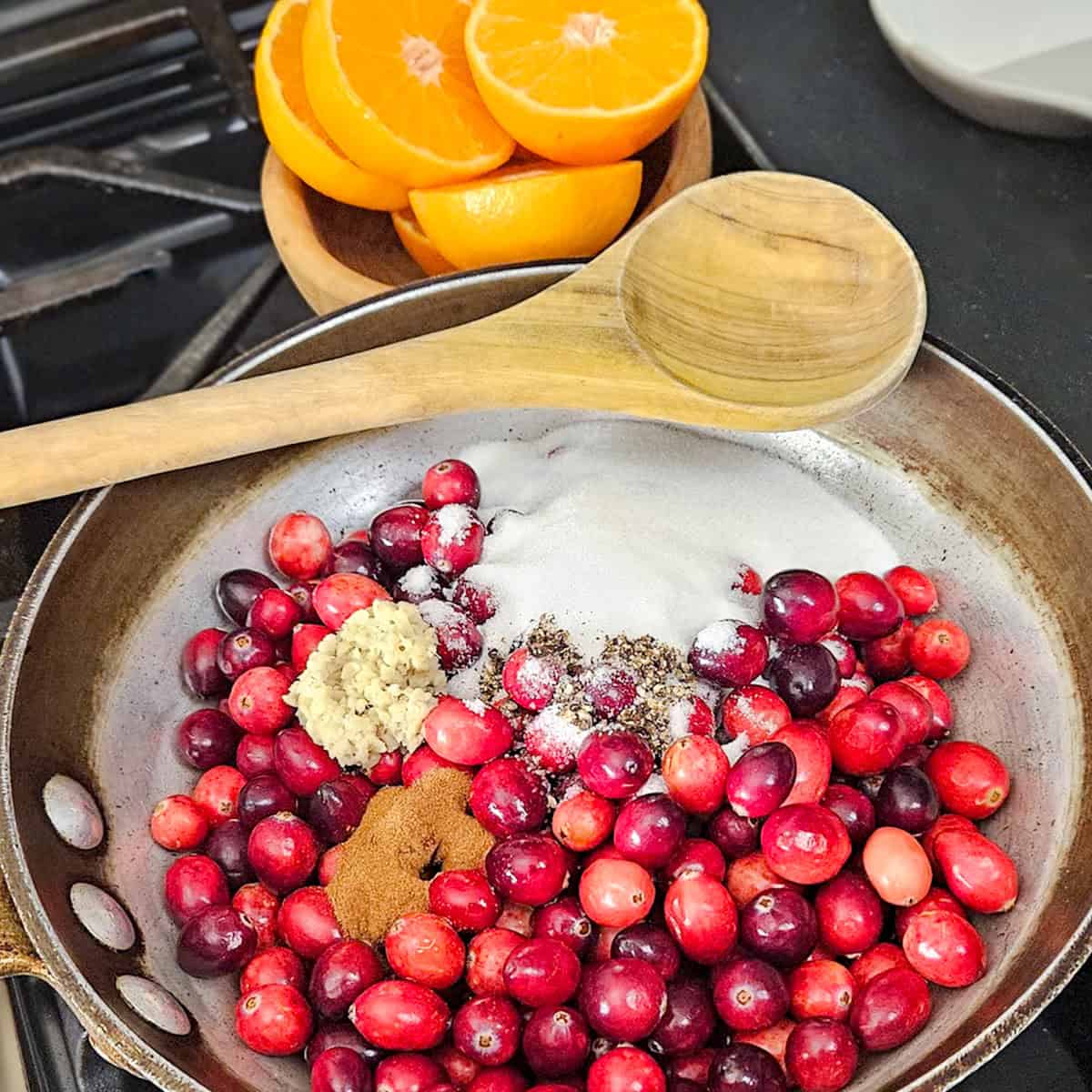 Fruity ingredients like cranberries, tangerine slices, ginger, and spices in a skillet. Perfect for seasonal cooking and flavor pairing.