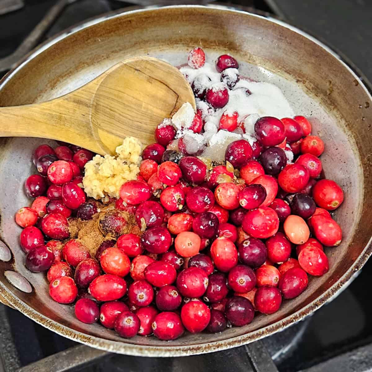 Juicy cranberries with ginger and spices cooking in a skillet for pomegranate cranberry sauce.