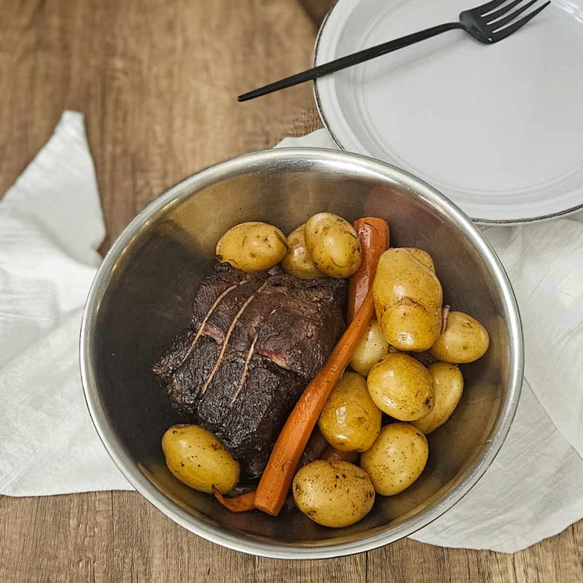 Delicious roast beef with potatoes and carrots, resting in a stainless steel bowl for a hearty meal.