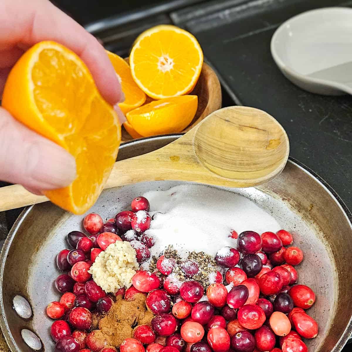 Close-up of cranberries and tangerines being juiced into a pan ready for cooking cranberry pomegranate sauce.