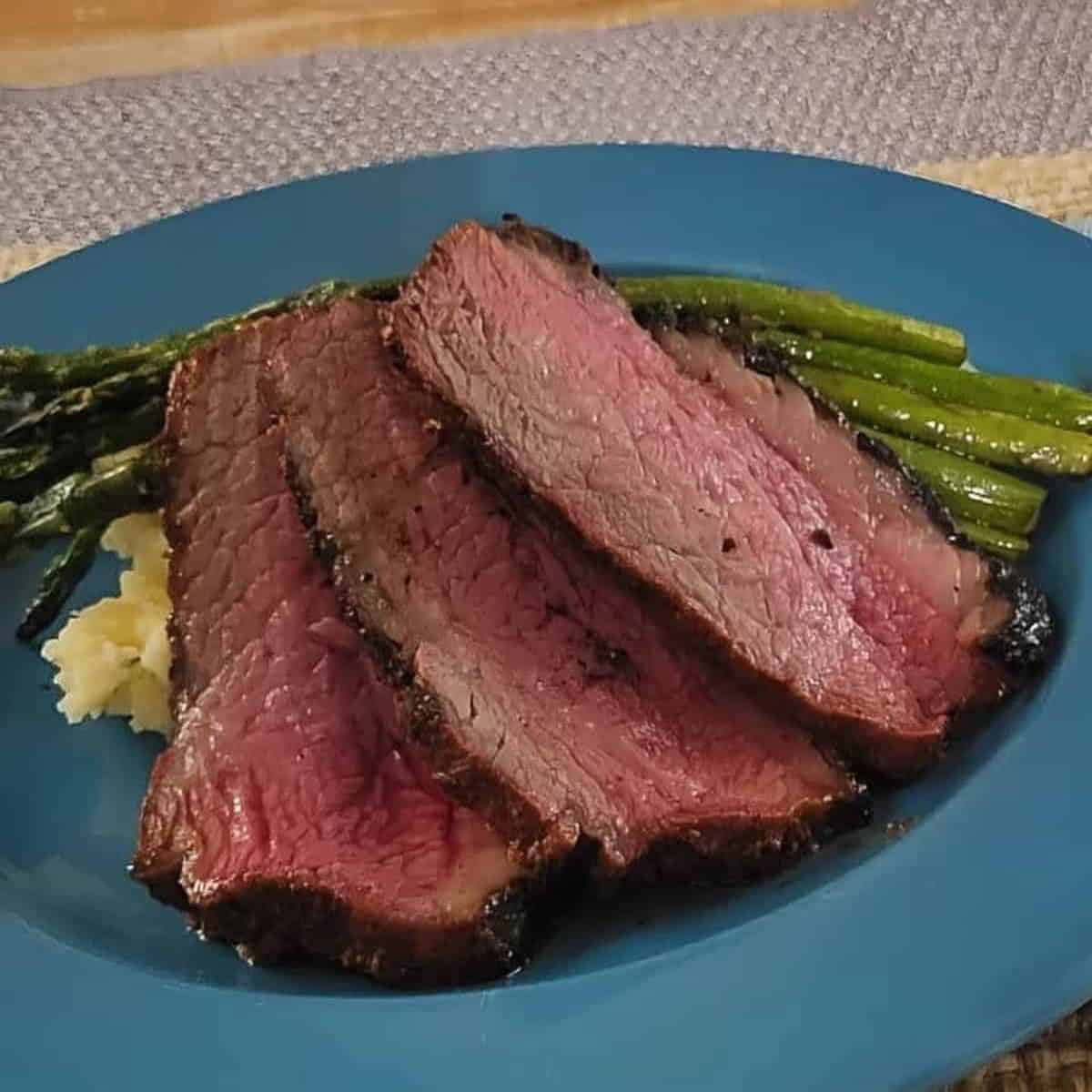 Sliced smoked beef tri tip roast on a plate with asparagus.