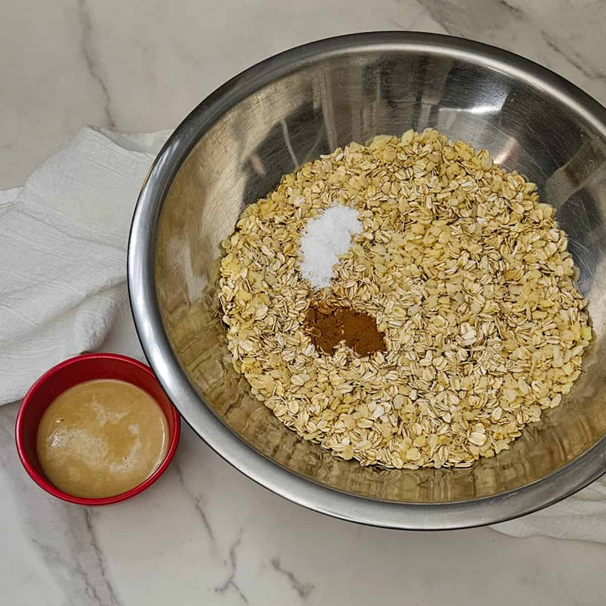 Oatmeal in a mixing bowl with salt, cinnamon, and chai and milk on a marble surface.