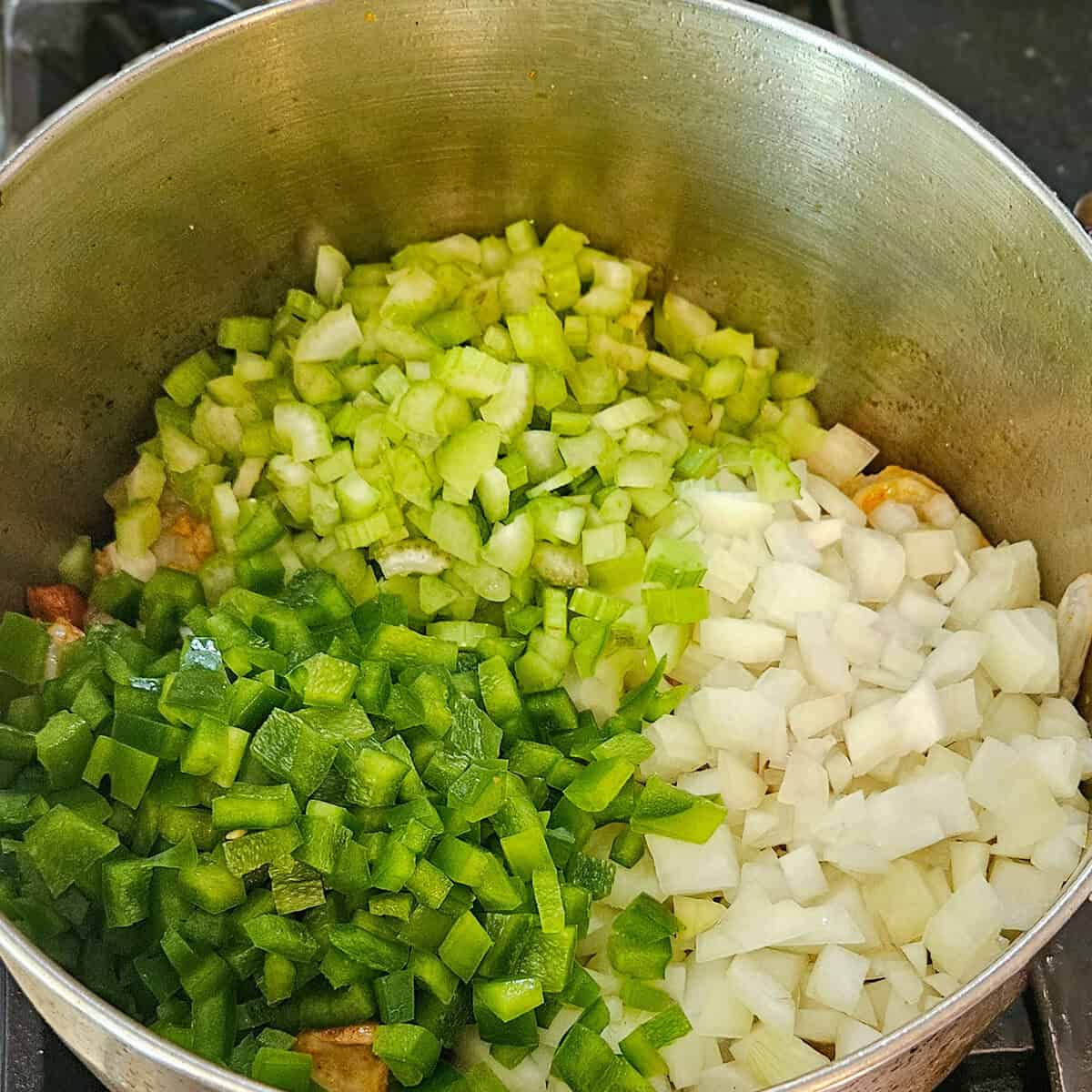 Adding celery, bell pepper, and onions to the pot on the stove for gumbo.