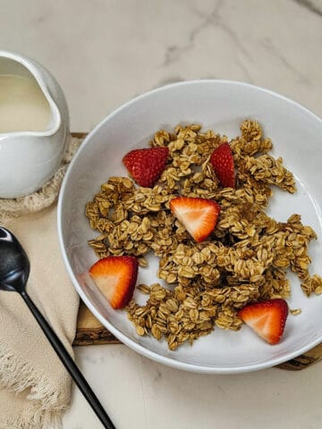 Crunchy homemade chai spice granola with fresh strawberries in a white bowl.