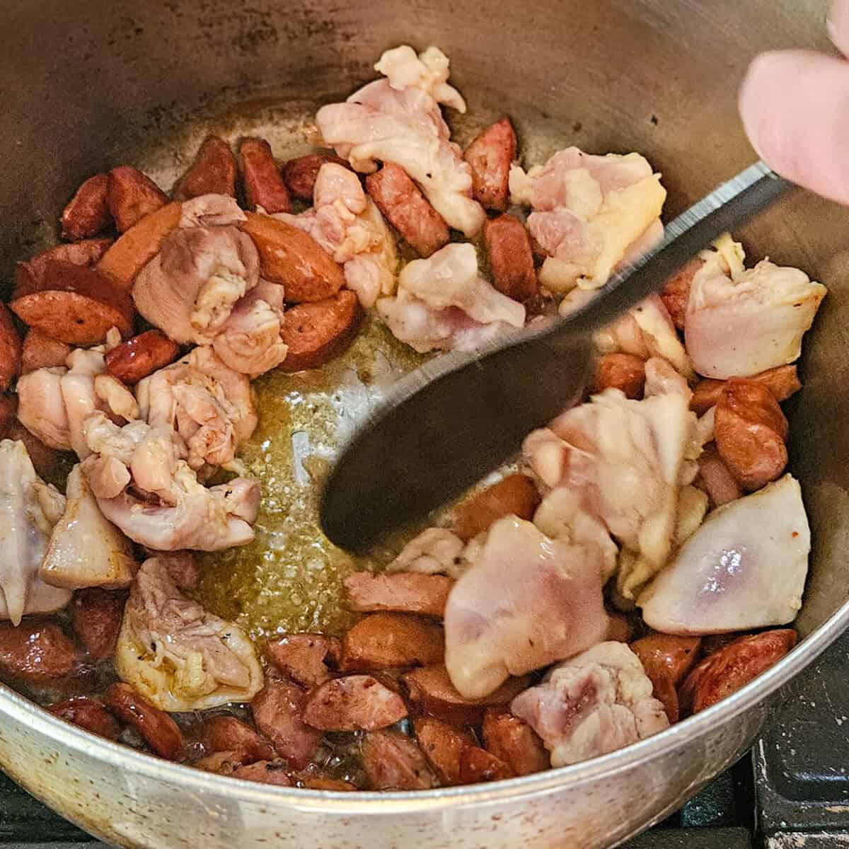 Stirring the sausage and chicken in a pot for the gumbo recipe.