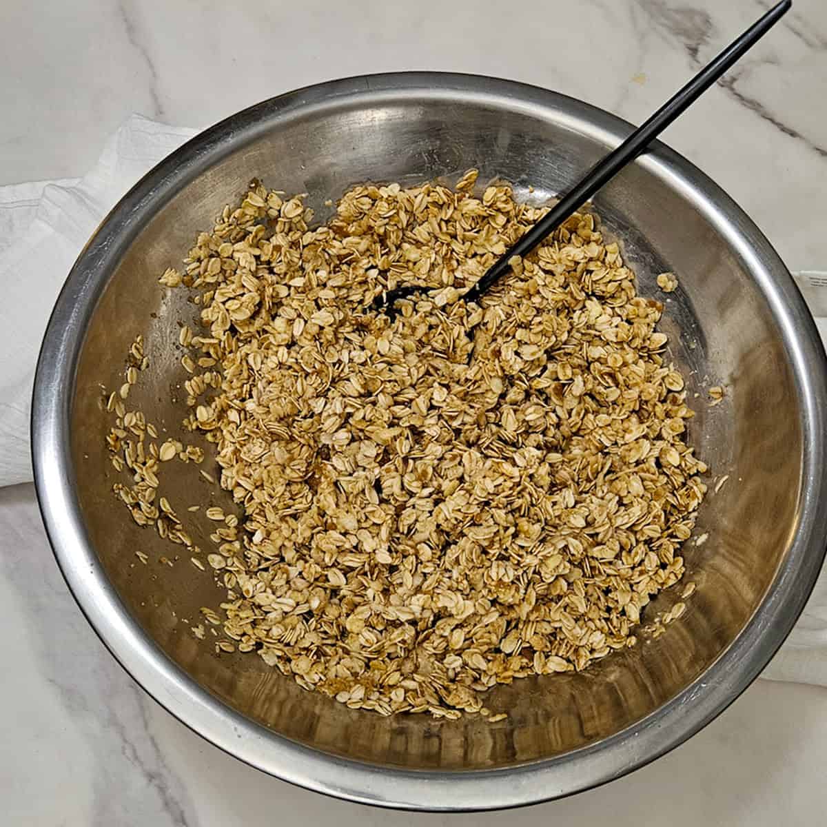 Mixing ingredients together for chai spice granola in a metal bowl.