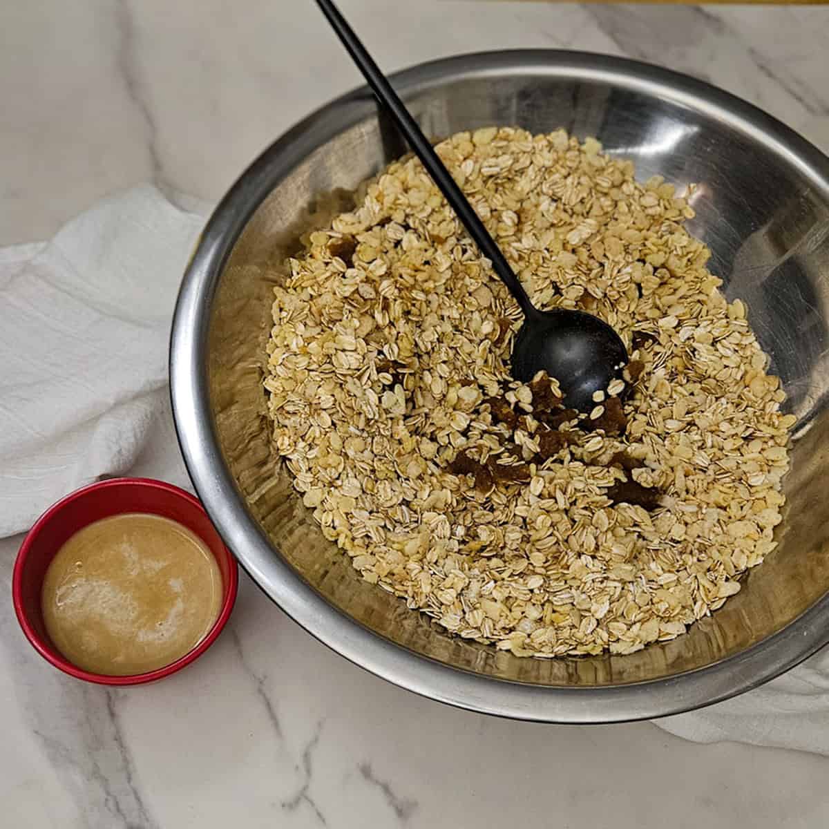 Mixing ingredients for chai spice granola in a metal bowl with chai tea and milk in a small bowl.